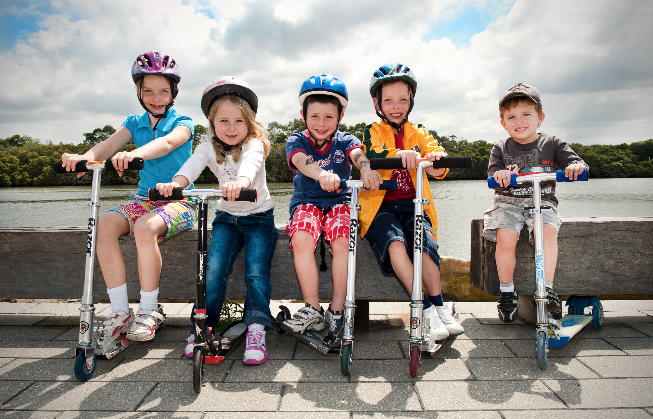 Five children with helmets and scooters looking directly at camera.