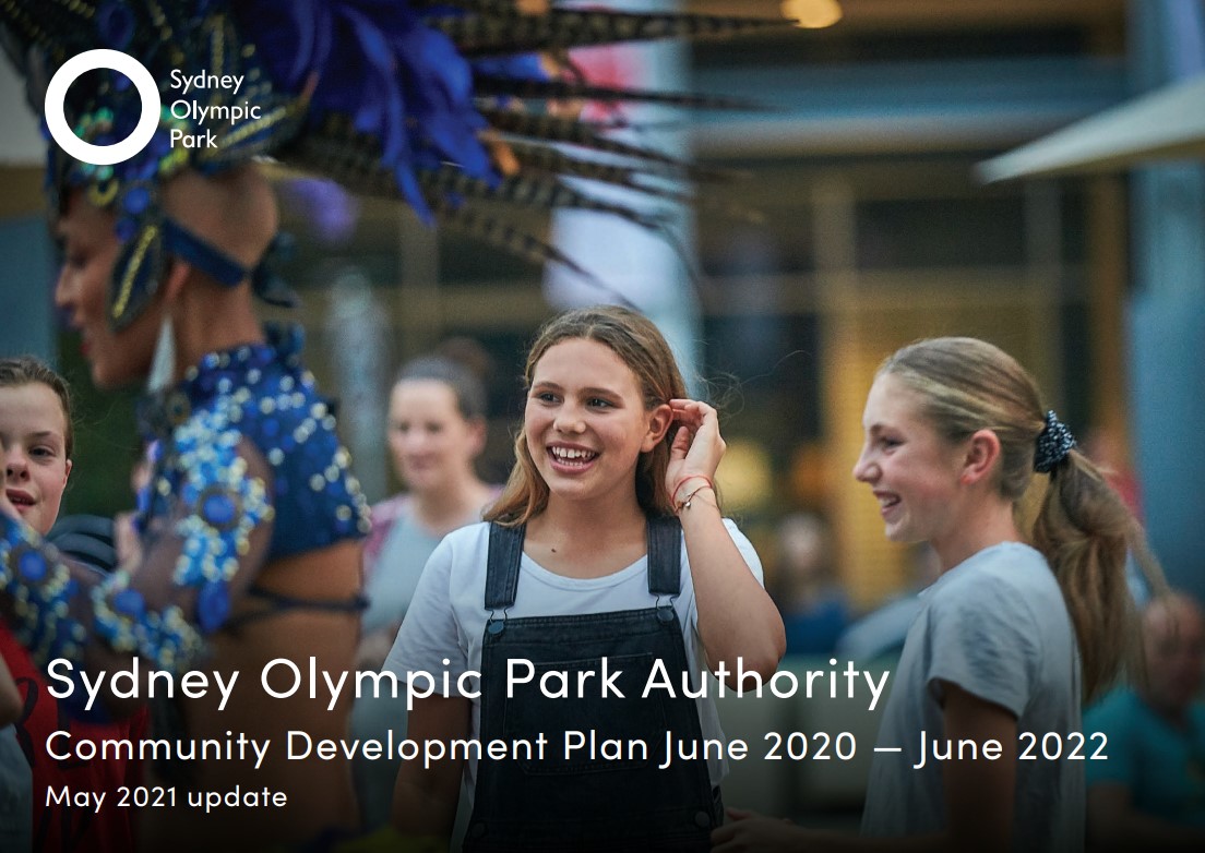 Cover of SOPA’s Community Development Plan June 2020 – June 2022 report which shows two young girls in a crowd enjoying watching a performer in elaborate dress go past.